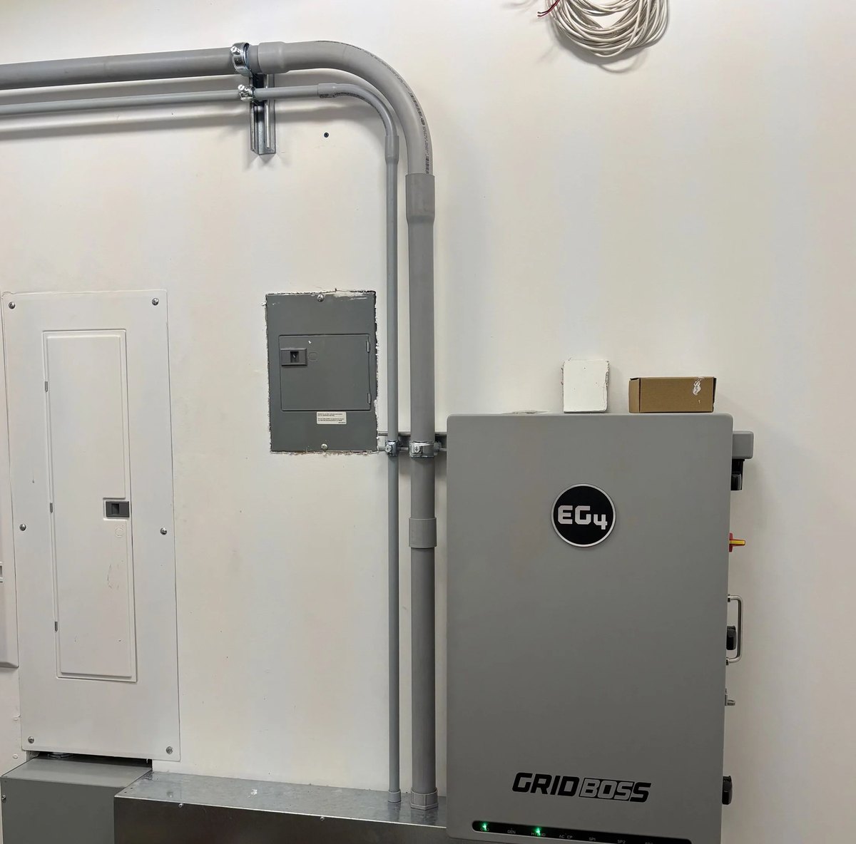 A service panel and a solar battery system wired in grey conduit on a white wall